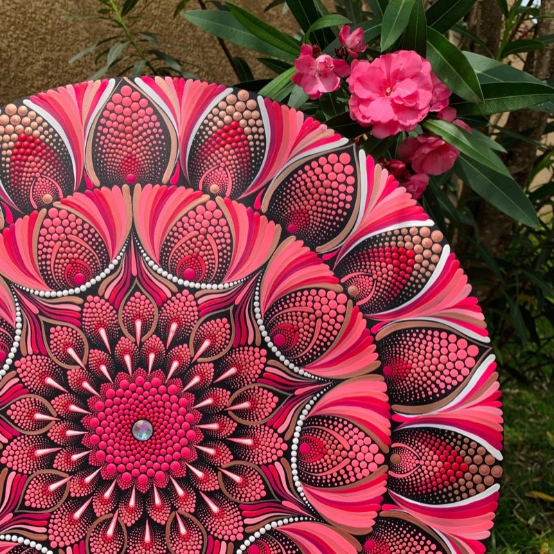Mandala em pontilhismo em tons de rosa e coral ao lado de flores